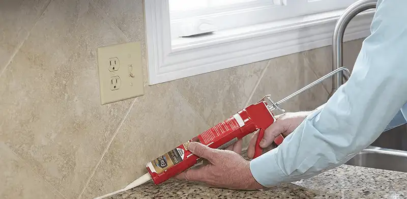 Handyman applying caulk along a kitchen backsplash and countertop seam in Boulder, CO