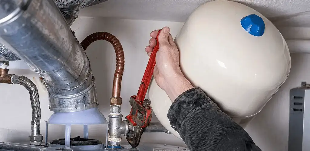 Water heater repair technician tightening plumbing connections near a tank unit in Boulder, CO